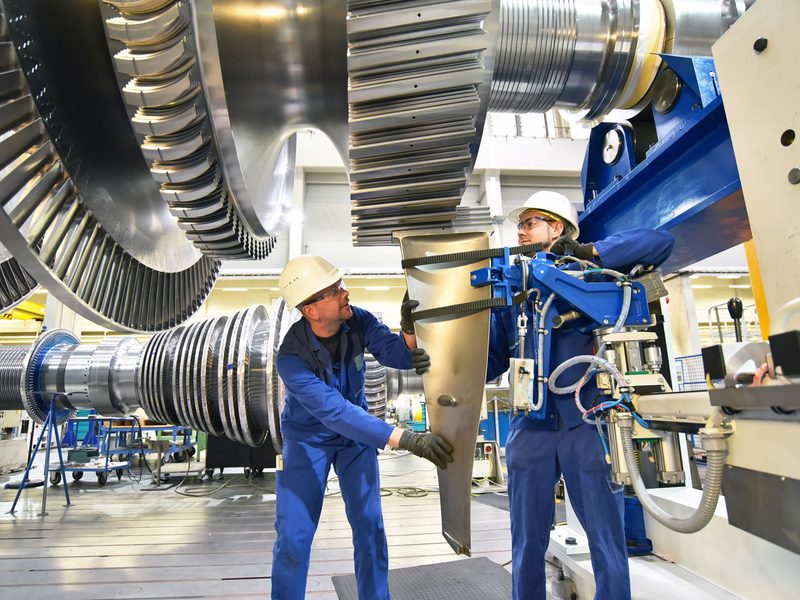 Two technicians in hard hats working on a large turbine